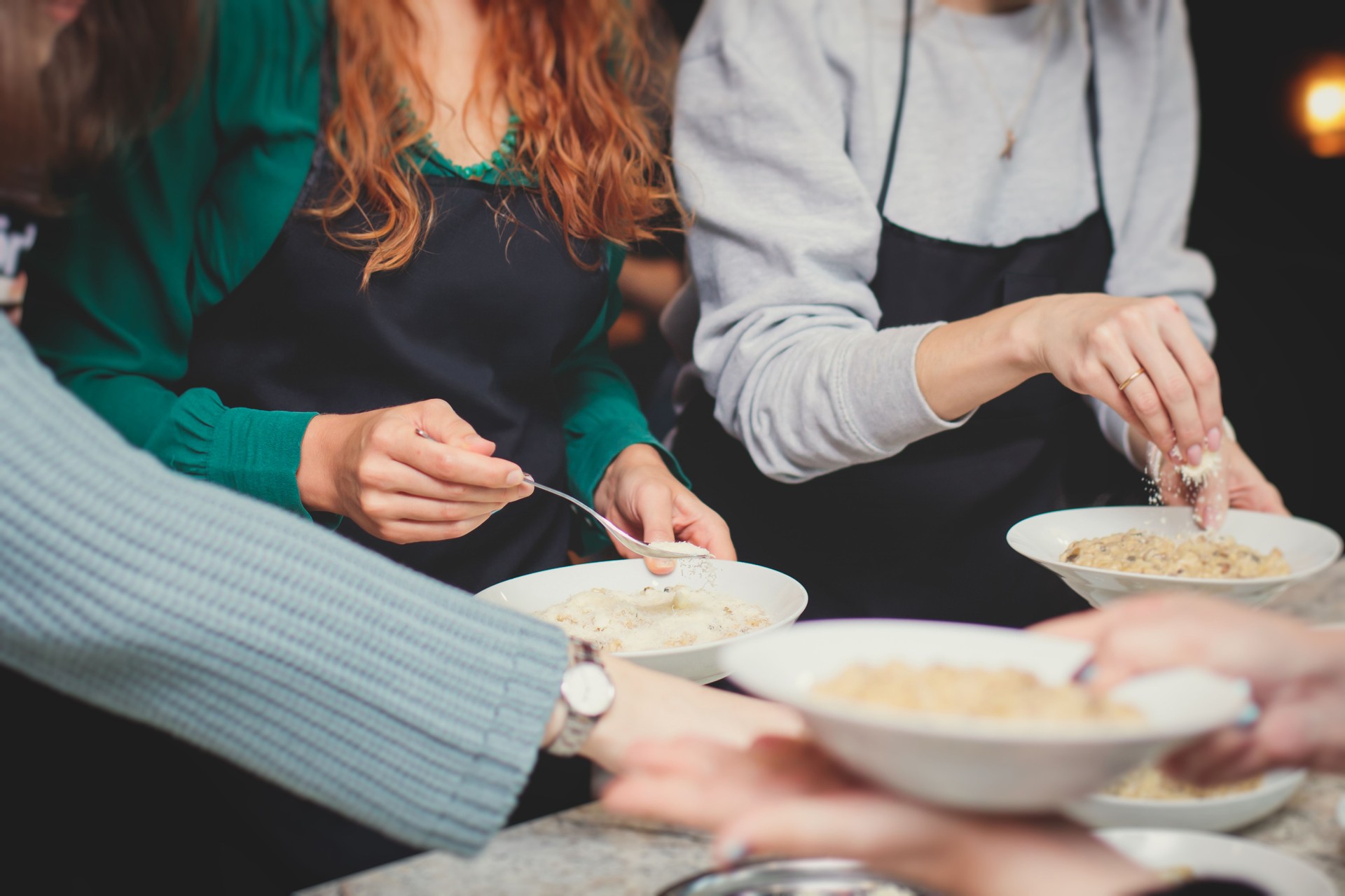 Group of people in a cooking class studio, adults preparing different dishes in the kitchen together, people in aprons learn on culinary master class, chef uniform, hands in gloves, italian cuisine