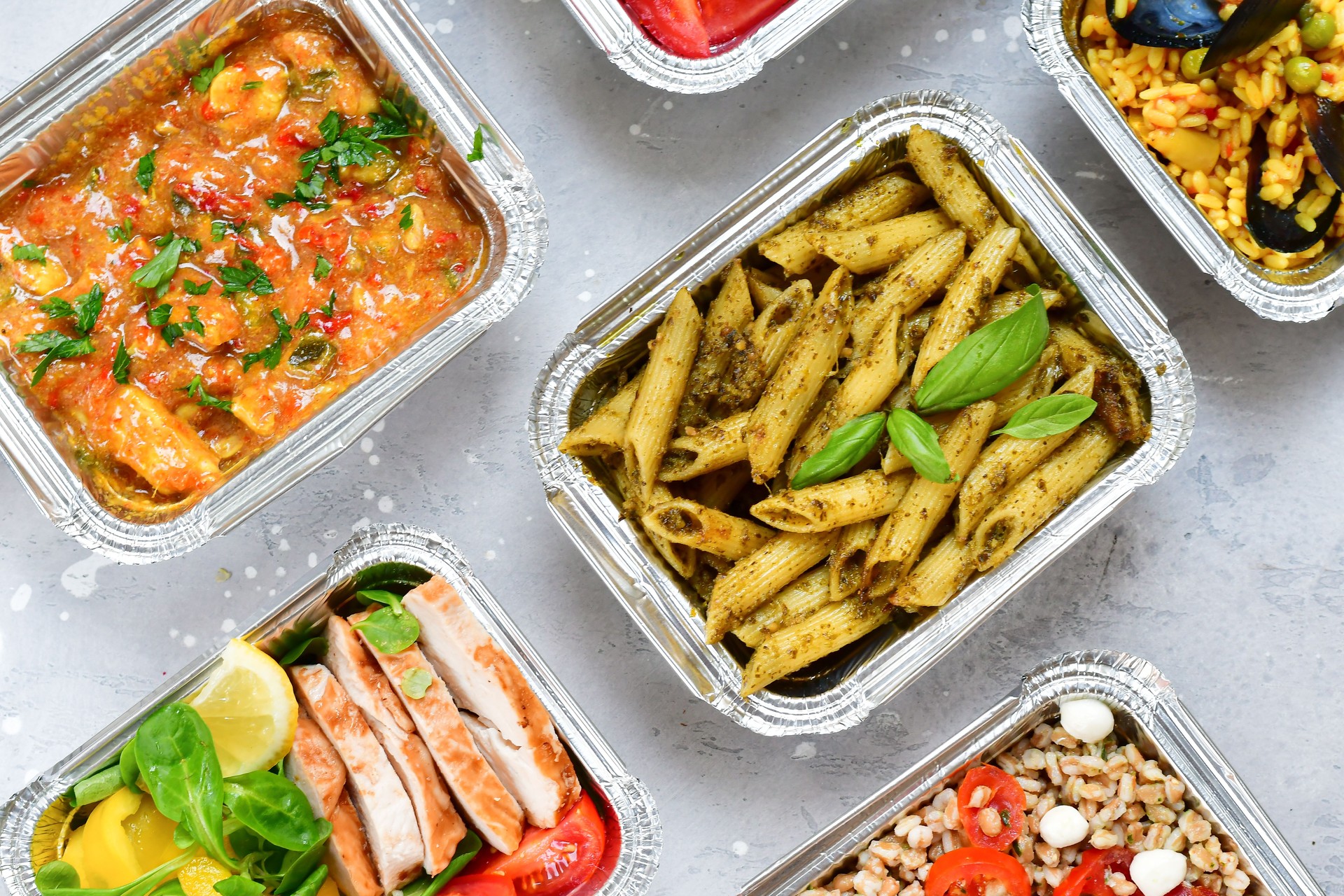 Different aluminium lunch box with healthy natural food pasta pesto, spelt, paella, quinoa, chicken salad, curry.